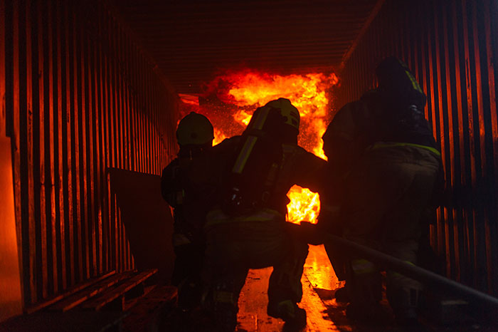 Firefighters run towards a burning building to rescue building occupants and contain/extinguish the fire.